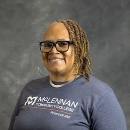 Smiling woman wearing glasses and a McLennan Community College T-shirt against a gray studio background.